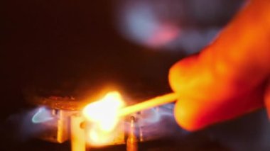 Ignite the gas on the stove with a matchstick in slow motion, close-up. Manual ignition of the gas burner in home kitchen. Burning blue flame of natural gas, macro. Burner operation, Fire on the stove
