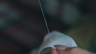 Genç kadın elleri yavaş çekimde iplik ve iğneyle elle dikilir, yakın çekimde. Manikürlü kadın parmakları evde günlük kıyafetlerle otururken dikiş dikiyor. Sıcak atmosfer, yaşam tarzı, el yapımı.