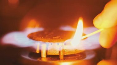 Ignite the gas on the stove with a matchstick, close-up. Manual ignition of the gas burner in home kitchen. Burning blue flame of natural gas, macro. Burner operation, Fire on the stove