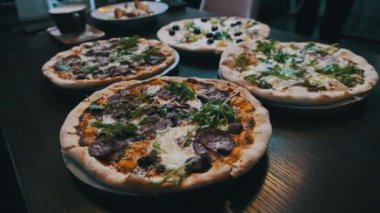 Pizzacıda bir sürü pizza var, yakın plan. Lokantada et, domuz pastırması, sucuk, peynir vb. ile iştah açıcı İtalyan pizzasından bol bol var. Çeşitli pizza çeşitleri. 4K