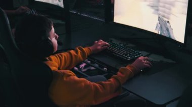 Bilgisayar kulübündeki bir çocuk oyun sandalyesinde oturup atış oyunu oynuyor. Esport Siber Kulübü 'nde kulaklık takan ve neon ışıkları video oyununa odaklanan bir genç. E-spor, hobi, sanal turnuva