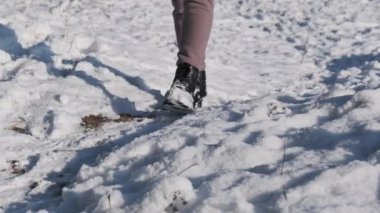View of women legs walking in the snow in slow motion. Female feets with winter shoes going by a snow-covered walkway in winter forest. Girl in black boots on snow. Winter time
