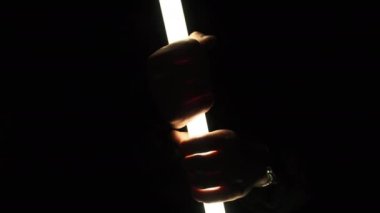 Erkeklerin elleri siyah arka planda hafif bir kılıç tutar. Erkek parmakları uzun, parlak bir LED boru feneri tutar. Neon ışın kılıcı. El fenerinden el silueti. 4K