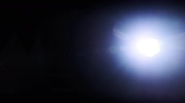 The light of a bright flashlight directed at the camera moves from side to side. Light effect of reflections in lenses. Flashes of blue light, effect. Transition, lens flare, light leaks. 4K