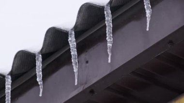 Icicles hang from the roof of a house in a winter day. Row of winter icicles hang from the overhang of the roof of the building against sky. Lot of icicles on the edge of house. 4K