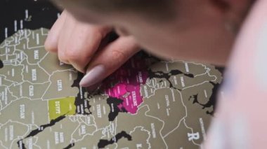 Woman scratching Europe countries on the surface of scratch world map in slow motion. Scratching visited countries on the travel map, close-up. Concept planning journey. Erase country on a scratch map