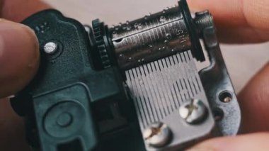 Old music box mechanism with spinning cylinder and cogs in male hands, macro. Retro music box clockwork device with rotating drum with projections touching the records creates music. Toy barrel organ.