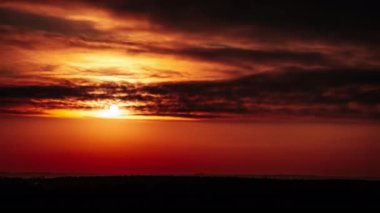 Timelapse of sunset in the orange sky behind the layered clouds over the horizon. Big bright red sun with sunrays moves down. Awesome epic cloud space, vibrant color. Time Lapse. Sundown. 4K