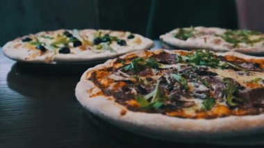 Pizzacıda bir sürü pizza var, yakın plan. Lokantada et, domuz pastırması, sucuk, peynir vb. ile iştah açıcı İtalyan pizzasından bol bol var. Çeşitli pizza çeşitleri. 4K