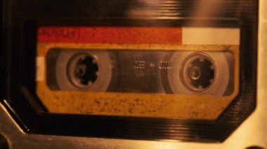 The cassette is played in a tape recorder in soft flickering candlelight, close-up. Yellow audio cassette in the deck rotates. Vintage sound recording in an old retro recorder. Audio Cassette playback