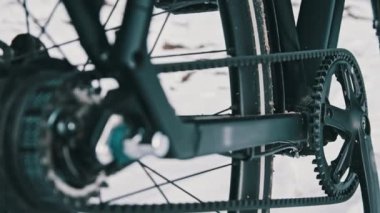 Belt drive transmission on a bicycle standing outdoors on the snow in a winter forest. Close-up of modern belt-drive instead of chain with a planetary hub. Toothed belt, gear change mechanism. 4K