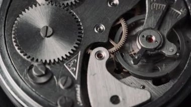 The mechanism of vintage stopwatch rotates close-up. Round clock watch mechanism working in a macro. Old retro clockwork gears, cogwheels, and pendulum movement inside the ancient clock. 4K