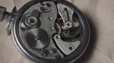 Clock mechanism rotates close-up. Vintage round stopwatch mechanism working in a macro. Old retro clockwork gears, cogwheels, and pendulum movement inside the ancient metal watch.