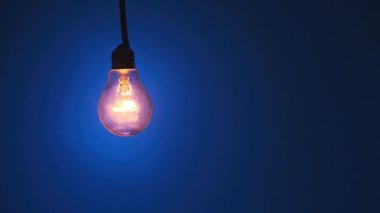 Kablodaki parlak lamba parlıyor ve koyu mavi arka planda yanıp sönüyor. Edison ampulü yavaşça açılıp kapanıyordu, yakın planda yanıp sönüyordu. Ilık yanıp sönen filament. Eski klasik ampul. Boşluğu kopyala, metin için yer