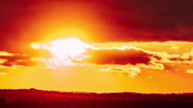 Timelapse of sunset in the orange sky behind the layered clouds over the horizon. Big bright red sun with sunrays moves down. Awesome epic cloud space, vibrant color. Time Lapse. Sundown. 4K