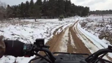 First-person view of a man riding a quad bike on snowy terrain, steering wheel view. POV control ATV on a snow-covered path in winter. Riding a four-wheeled in a snowy area. Vocation, off-road racing