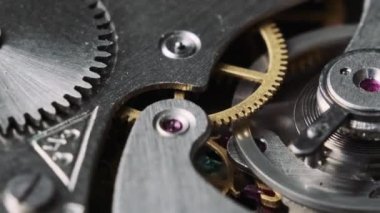 Clock mechanism rotates close-up. Vintage round stopwatch mechanism working in a macro. Old retro clockwork gears, cogwheels, and pendulum movement inside the ancient metal watch.