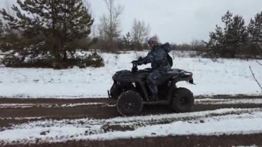 Kışın karla kaplı bir patikada bisiklete binen bir kadın. Kar manzarası boyunca ATV bisikleti sürmek. Karlı bir alanda dört tekerlekli bir ATV 'ye binmek. Kış tatili Off-road yarışı. Yaşam tarzı 4K 50 fps