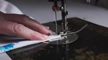 Old female hands of seamstress sew at a retro sewing machine at home in slow motion. Close-up of aged female fingers sewing fabric at a traditional sewing machine. The needle quickly moves up and down