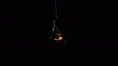Yanan lamba yanıyor ve siyah arka planda yanıp sönüyor. Yakından bir ampul açıp kapadı. Ilık yanıp sönen filament. Tungsten ampul ışığı ve klasik ışığın rahat parlaklığı. Fikir, kopyalama alanı. 4K