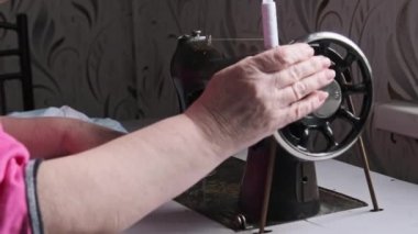 An old seamstress sews on a vintage sewing machine at home. Needle for retro sewing machine in slow motion. The process of sewing the fabric. Close-up of grandmother hands working at a sewing machine