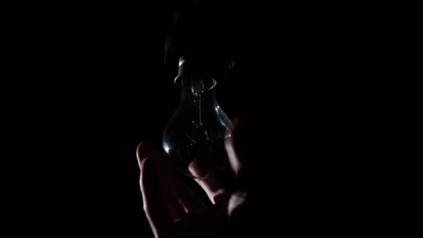 Male Hand Twists Incandescent Bulb Socket Glows Flickers Black Background — Vídeo de Stock