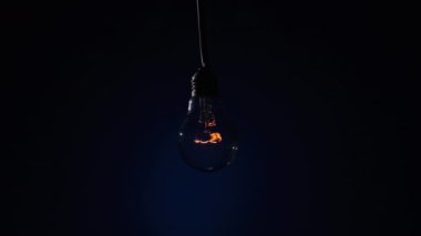 Parlayan lamba koyu mavi arka planda parlıyor ve yanıp sönüyor. Edison ampulü yavaşça açılıp kapanıyordu. Yakından yanıp sönüyordu. Ilık yanıp sönen filament. Retro klasik ampul. Boşluğu kopyala, metin için yer