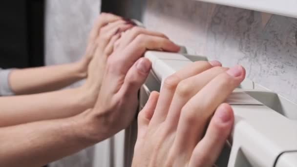 两只手放在墙边的暖气散热器上取暖 冰冷的男性和女性的手触摸家庭取暖电池 并试图加热 寒冷季节回家取暖的问题 供热系统差 — 图库视频影像
