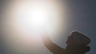 Zayıf cep telefonu sinyali. Kışlık giysiler içindeki genç bir kızın silueti mavi gökyüzündeki parlak güneşi engelleyen bir akıllı telefonu kaldırıyor. Ağ ararken kayıp cep telefonu sinyalini yakala