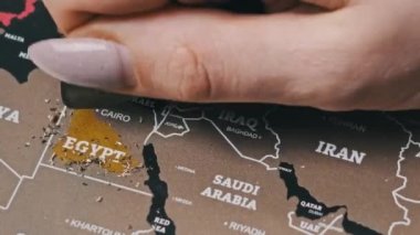 Scratching Egypt Country on the Surface of Scratch World Map. Woman hand erases visited countries on the travel map. Scratch a world map with many countries, close-up. Concept of the planning journey