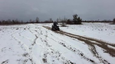 Kışın karla kaplı bir patikada bisiklete binen bir kadın. Kar manzarası boyunca ATV bisikleti sürmek. Karlı bir alanda dört tekerlekli bir ATV 'ye binmek. Kış tatili Off-road yarışı. Yaşam tarzı 4K 50 fps