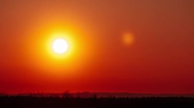 Timelapse of sunset in the orange sky over the horizon. Big bright red sun with sunrays moves down in a light evening haze. Awesome epic cloud space, vibrant color. Time Lapse. Sundown. 4K