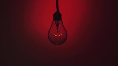 Koyu kırmızı arka planda parlak ve yanıp sönen bir lamba. Edison ampulü yavaşça açılıp kapanıyordu. Yakından yanıp sönüyordu. Ilık yanıp sönen filament. Retro klasik ampul. Boşluğu kopyala, metin için yer