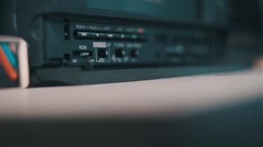 Insert VHS cassette into VCR player. Black vintage videotape cassette recorder on a desk with many archived video cassettes. Female hand inserting old VHS Tape into retro player. Home video, nostalgia