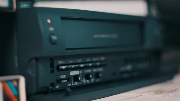 VhsカセットをVcrプレーヤーに挿入します 多くのアーカイブされたビデオカセットを持つ机の上に黒いヴィンテージのビデオテープカセットレコーダー レトロなプレーヤーに古いVhsテープを挿入男性の手 ホームビデオ — ストック動画