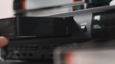 Male hand inserts VHS cassette into a VCR Video recorder. Black vintage videotape cassette recorder on a desk with many video cassettes. Inserting old VHS Tape into a retro player. Home video archive