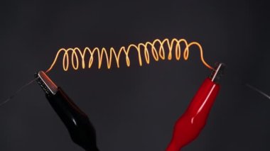 Nichrome filament connected to power wires is heated to red under the influence of a large current. Electric spiral wire heater heating the air and glowing. High metal resistance. Electric strength.