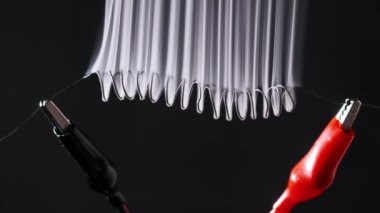 Nichrome wire heats up to red with smoke under a high electric current, slow motion. Nichrome filament in the form of spiral connected to power wires. Close-up, high metal resistance. Current strength