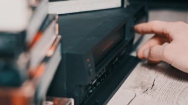 Erkek eli, eski bir video kayıt cihazından VHS çekiyor. Arşivlenmiş video kasetlerin olduğu bir masadaki bir video oynatıcıdan VHS kaseti çıkar. VHS retro oynatıcı. Ev videosu kavramı, eski teknoloji