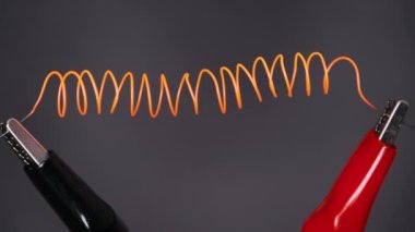 Nichrome filament glowing to red under high electric current. Nichrome thread in the form of a spiral connected to power wires. Wire glowing, high metal resistance. Current strength. Lab test Close-up