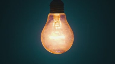 Incandescent lamp on wire glows and flickers on dark blue background. Edison bulb slowly turned on and off, pulsing light close-up. Warm flashing filament. Old classic bulb. Copy space, place for text