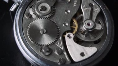 The mechanism of vintage stopwatch rotates close-up. Round clock watch mechanism working in a macro. Old retro clockwork gears, cogwheels, and pendulum movement inside the ancient clock. 4K