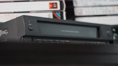 VHS kaseti VCR 'a ekle. Masasında bir sürü video kaseti olan siyah antika bir kaset kaydedici. Eski VHS bandı retro oynatıcıya yerleştiriliyor. Ev video arşivi
