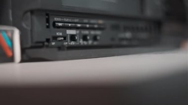 Kadın eli VHS kaseti bir video kaydediciye yerleştiriyor. Masada bir sürü video kasetçalar ve siyah antika kasetçalar var. Antika çalgıcıya retro VHS bandı yerleştiriliyor. Ev videosu