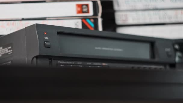 VhsカセットをVcrに挿入します 多くのビデオカセットと机の上にカウンターと黒のヴィンテージのビデオテープカセットレコーダー レトロなプレーヤーに古いVhsテープを挿入します ホームビデオアーカイブ — ストック動画