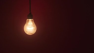 Incandescent lamp glows and flickers on dark Red background. Edison light bulb slowly turned on and off, pulsing light close-up. Warm flashing filament. Retro classic bulb. Copy space, place for text