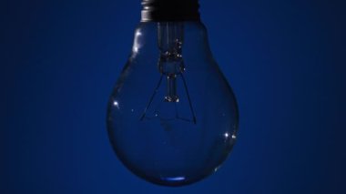 Parlayan lamba koyu mavi arka planda parlıyor ve yanıp sönüyor. Edison ampulü yavaşça açılıp kapanıyordu. Yakından yanıp sönüyordu. Ilık yanıp sönen filament. Retro klasik ampul. Uzaklaştır