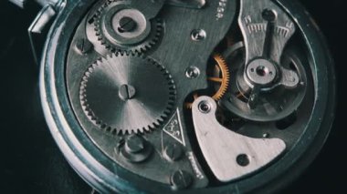 Clock mechanism rotates close-up. Vintage round stopwatch mechanism working in a macro. Old retro clockwork gears, cogwheels, and pendulum movement inside the ancient metal watch.