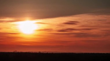 Timelapse of sunset in the orange sky behind the layered clouds over the horizon. Big bright red sun with sunrays moves down. Awesome epic cloud space, vibrant color. Time Lapse. Amazing sundown. 4K