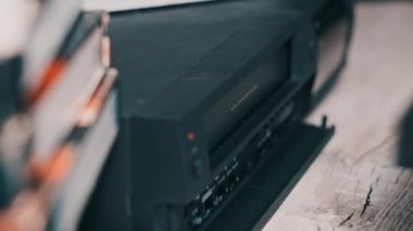Insert VHS cassette into VCR player. Black vintage videotape cassette recorder on a desk with many archived video cassettes. Male hand inserting old VHS Tape into a retro player. Home video, nostalgia